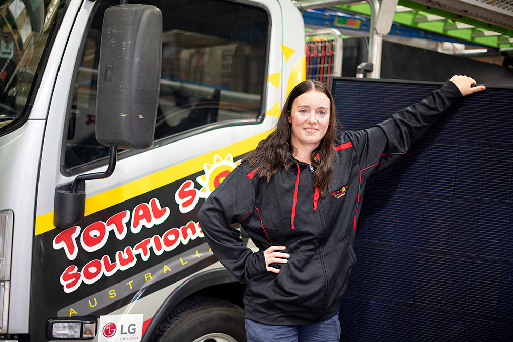 Madi standing infront of a solar panels and work truck